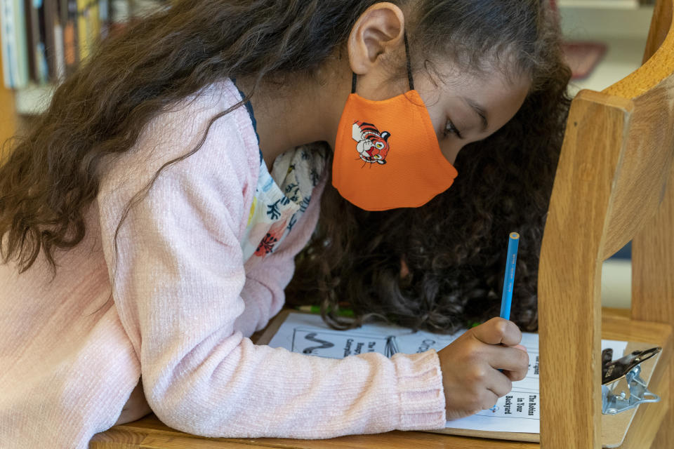 A first grader wears a face mask while doing work in the library during the coronavirus outbreak at the Post Road Elementary School, Thursday, Oct. 1, 2020, in White Plains, N.Y. (AP Photo/Mary Altaffer)