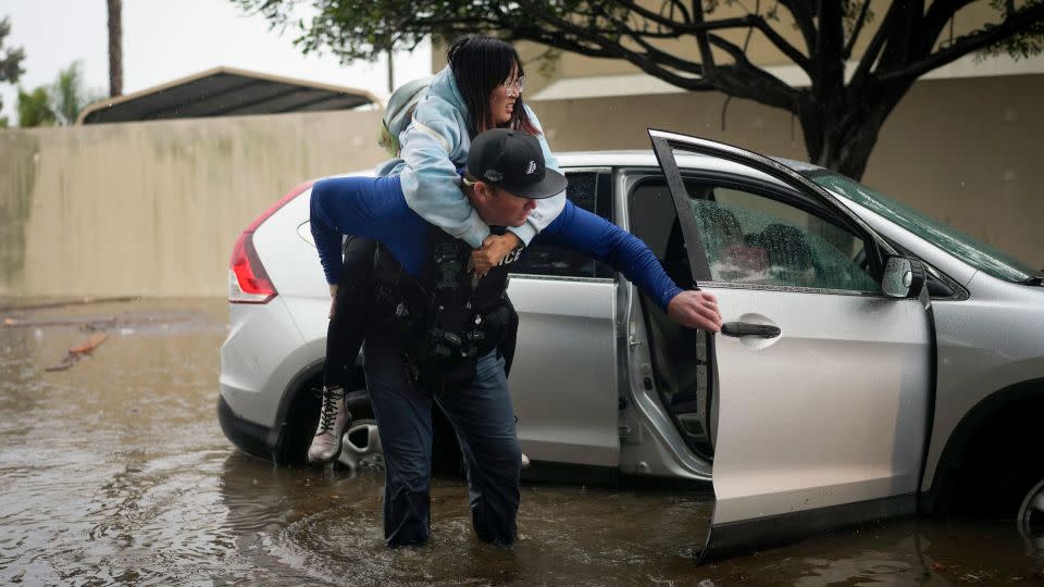 Det. Bryce Ford of the Santa Barbara, California, Police Department helps a motorist out of her car on a flooded street during a rainstorm. - Jae C. Hong/AP