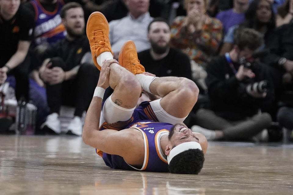 Phoenix Suns guard Devin Booker (1) holds his leg after injuring it during the second half of an NBA basketball game against the Houston Rockets in Phoenix, Saturday, March. 2, 2024. (AP Photo/Darryl Webb)