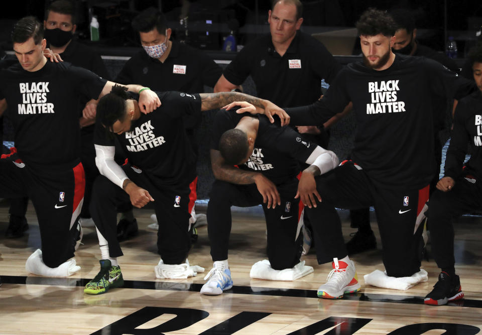 Portland Trail Blazers' Damian Lillard, second from right, the kneels with teammates and coaches during the national anthem before an NBA basketball game against the Memphis Grizzlies, Friday, July 31, 2020, in Lake Buena Vista, Fla. (Mike Ehrmann/Pool Photo via AP)