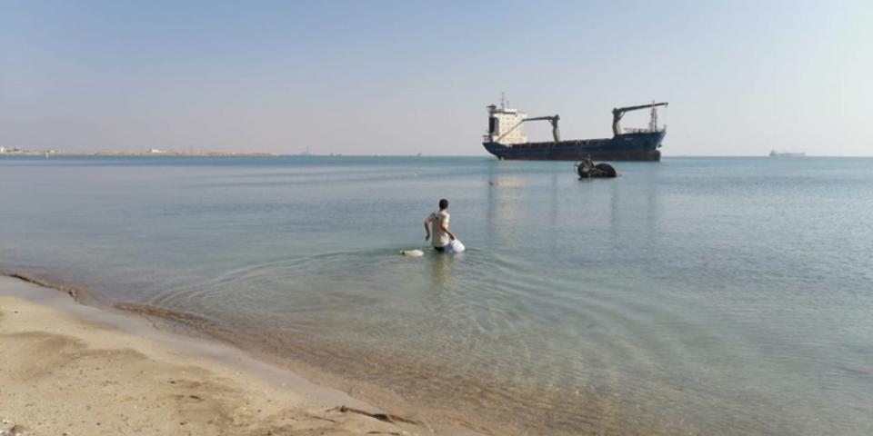 Seafarer Mohammad Aicha wades from a beach towards a ship on the horizon, the MV Aman.