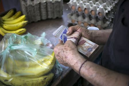 A clerk counts Venezuelan bolivar banknotes after selling goods to a customer at a fruit and vegetable store in Caracas July 10, 2015. REUTERS/Marco Bello
