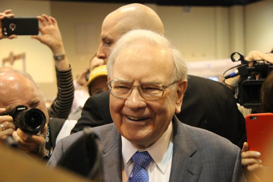 Warren Buffett smiles as he is surrounded by people with cameras trained on him.