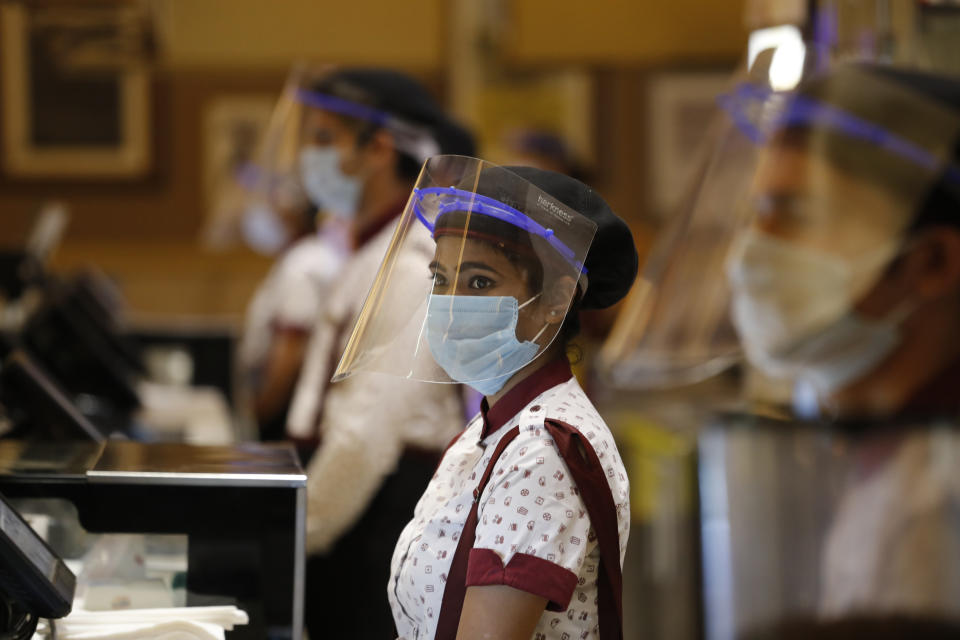 Workers of PVR cinemas, a multiplex cinema chain, stand at the food court with face shields and masks during a press preview to show their preparedness with the COVID-19 pandemic in New Delhi, India, Friday, July 31, 2020. (AP Photo/Manish Swarup)