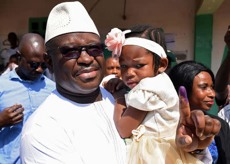 FILE PHOTO: Julius Maada Bio, the presidential candidate for the Sierra Leone People's Party (SLPP), carries his daughter as he shows his ink-stained finger after casting his vote during Sierra Leone's general election in Freetown, Sierra Leone March 7, 2018. REUTERS/Olivia Acland