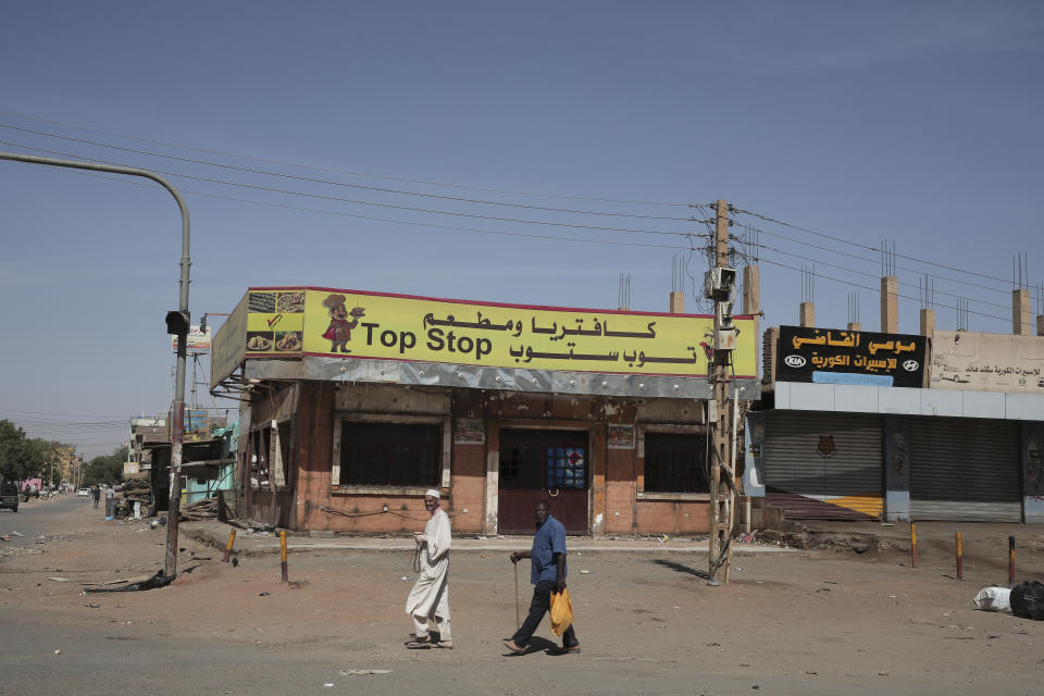 People walk past shuttered shops in Khartoum, Sudan, Tuesday, April 18, 2023. Sudan's embattled capital has awoken to a fourth day of heavy fighting between the army and a powerful rival force for control of the country. Airstrikes and shelling intensified on Monday in parts of Khartoum and the adjoining city of Omdurman. (AP Photo/Marwan Ali)