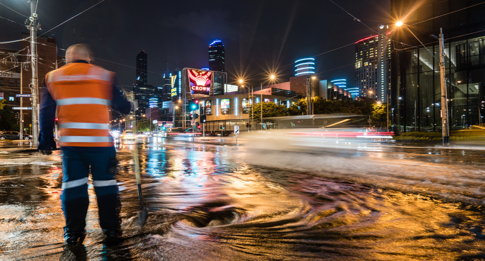 Flooded Melbourne streets with a man in hi-vis in the foreground.