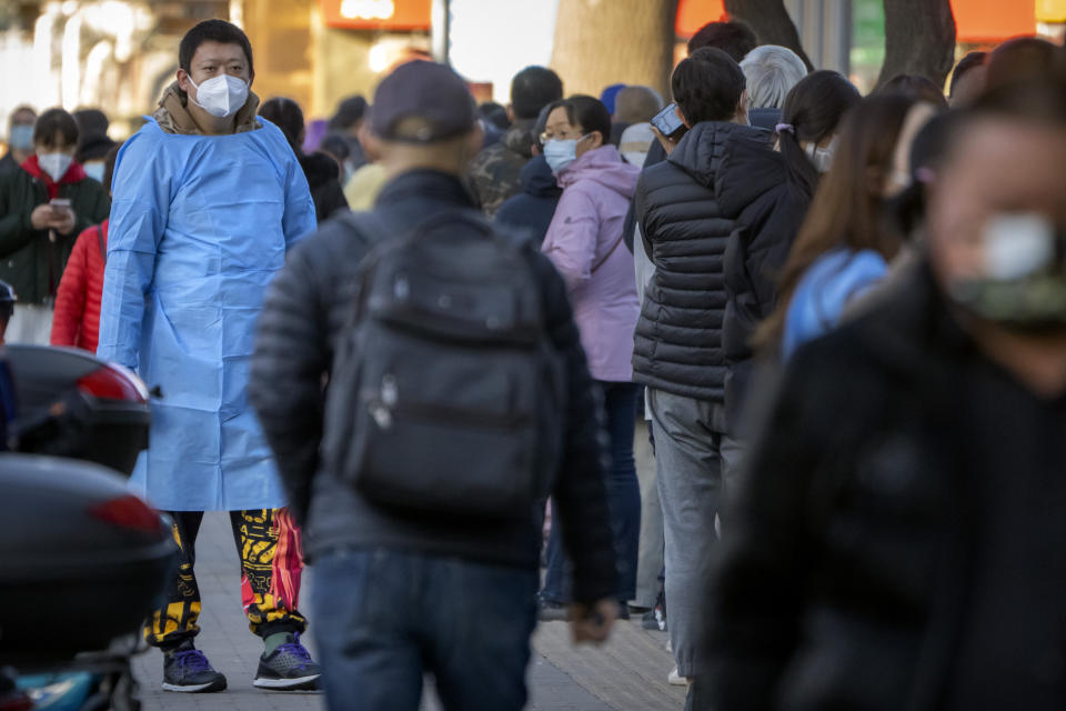 A worker wearing protective clothing watches as people stand in line for COVID-19 tests at a coronavirus testing site in Beijing, Tuesday, Nov. 15, 2022. The flagship newspaper of China's ruling Communist Party has called for strict adherence to the country's hardline "zero-COVID" policy, in an apparent attempt to guide public perceptions following a slight loosening of anti-virus regulations. (AP Photo/Mark Schiefelbein)