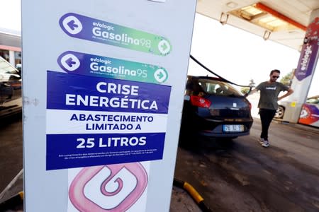 FILE PHOTO: A placard reading "Energy crisis. Maximum limit 25 litres per filling" is seen as a man fills up a car during a fuel strike, at a gas station near Lisbon