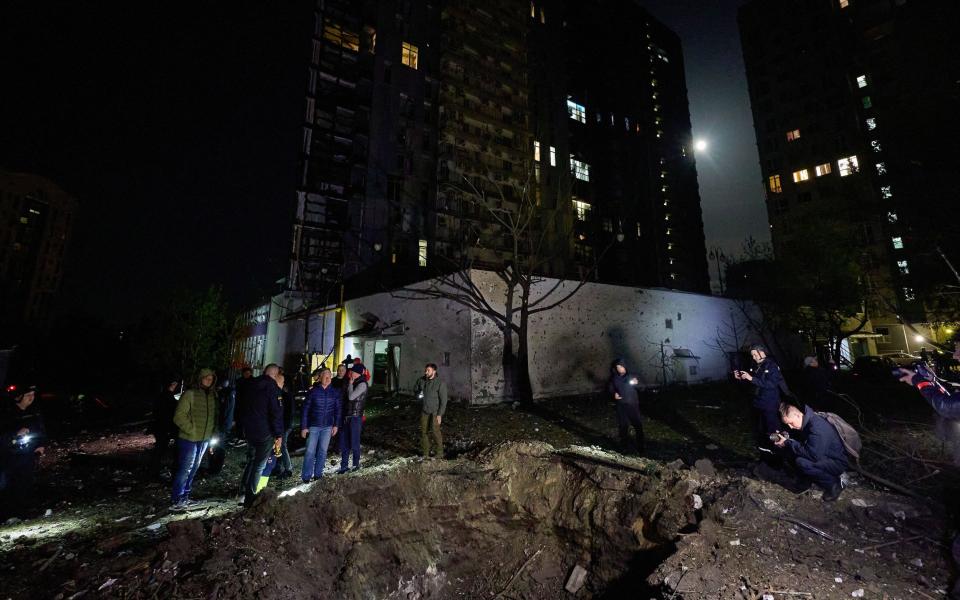 People stand near the edge of a shell crater among residential buildings after shelling in Kharkiv, northeastern Ukraine.