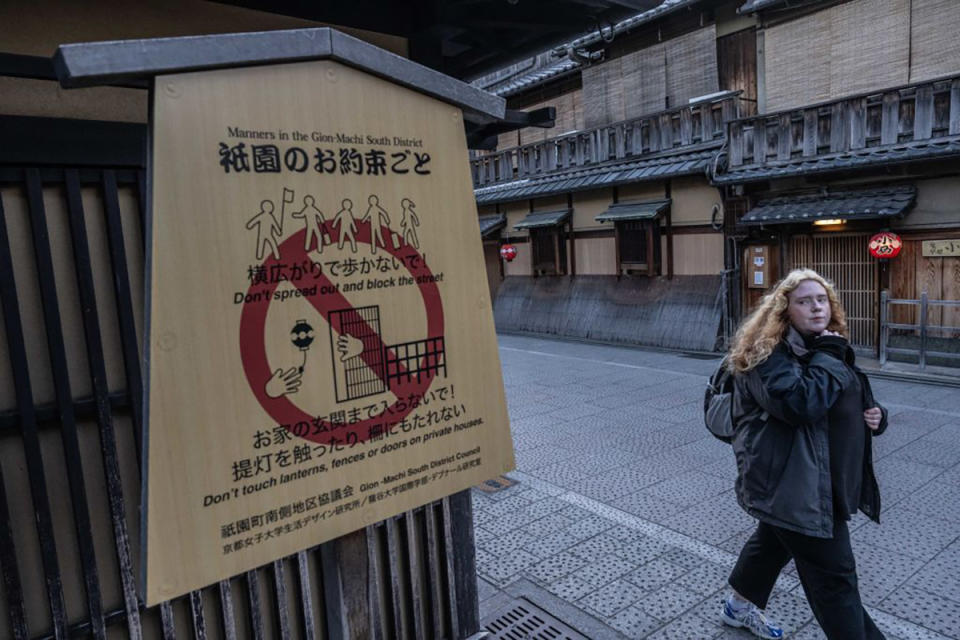 A woman walks past a sign saying 