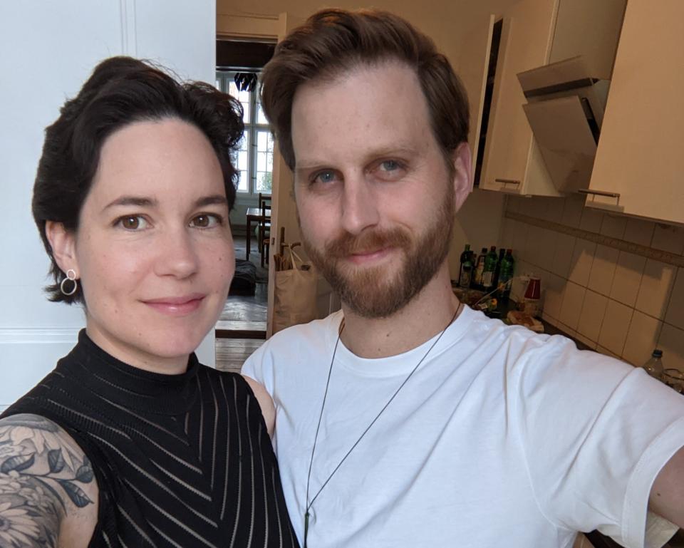 The author, left, and her husband. They are standing in their kitchen and smiling into the camera. She has a black tank top on and he is wearing a white t-shirt.