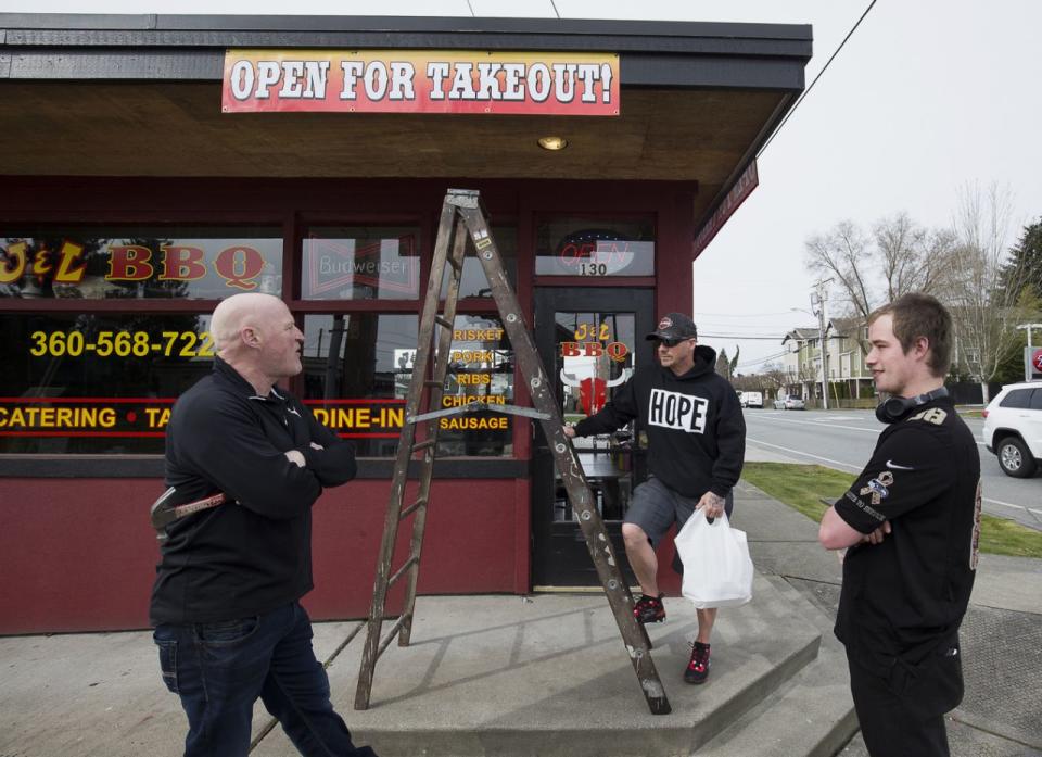 El dueño de J & L BBQ, Joel Sexton, a la izquierda, habla con los clientes Tony Cecsarini y Austin Eisenhuth, a la derecha, después de colgar unos carteles para anunciar que el restaurante acepta pedidos para llevar. La foto fue tomada el martes, 17 de marzo de 2020, en Snohomish, Washington (Andy Bronson / The Herald a través de AP).  