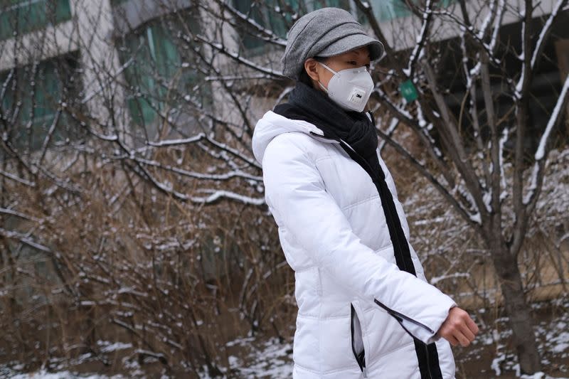 A woman wearing a face mask walks at a residential complex after a snowfall, as the country is hit by an outbreak of the new coronavirus, in Beijing