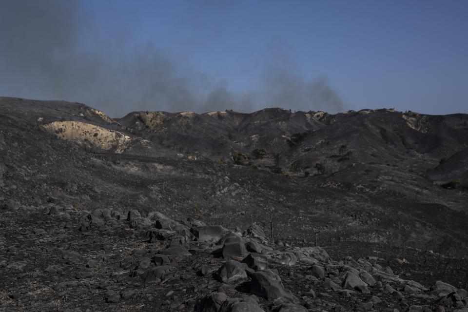 Smoke rises behind a burnt forest in Asklipio village, on the Aegean Sea island of Rhodes, southeastern Greece, on Wednesday, July 26, 2023. A third successive heat has struck Greece, amid more evacuations from fires that have raged out of control for days, while the temperature in many parts of the country soaring Wednesday to as high as 46.4C (115 Fahrenheit). (AP Photo/Petros Giannakouris)