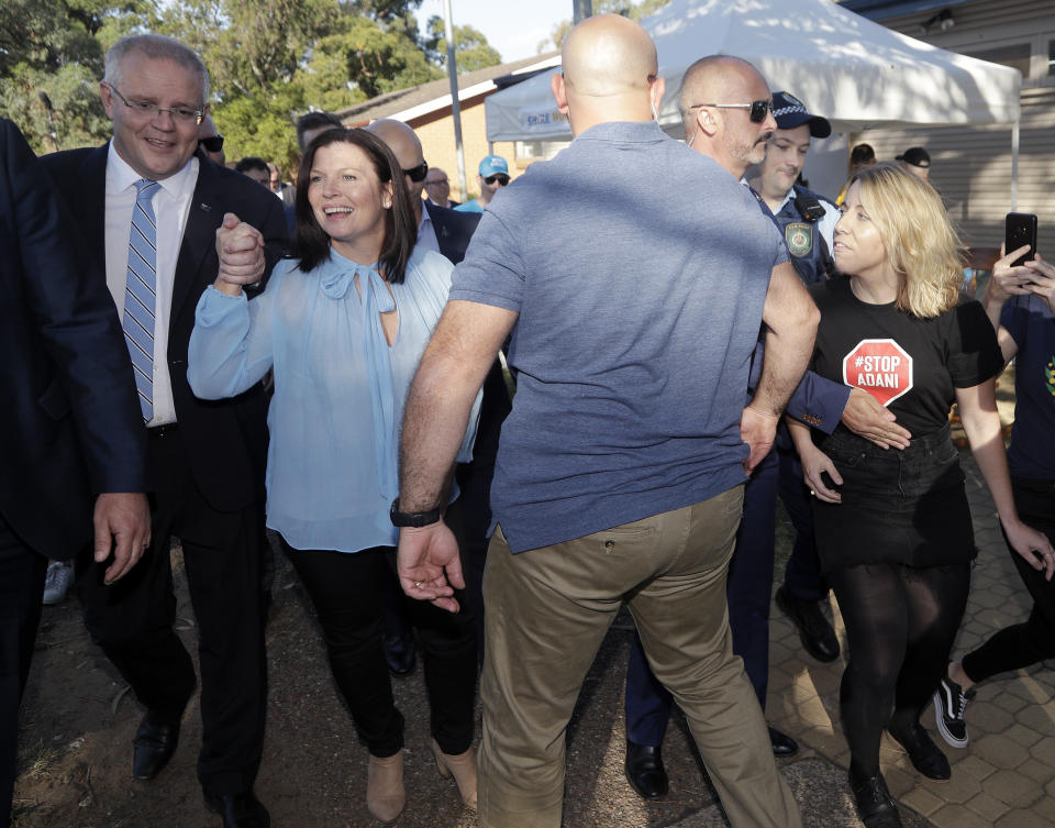 Australian Prime Minister Scott Morrison, left, holds his wife's, Jenny, hand as an anti-coal mining protester runs in from the right after Morrison voted in a federal election in Sydney, Australia, Saturday, May 18, 2019. Both major parties are promising that whoever wins the election the leader will remain prime minister until he next faces the voters' judgment. The parties have changed their rules to make the process of lawmakers replacing a prime minister more difficult. (AP Photo/Rick Rycroft)