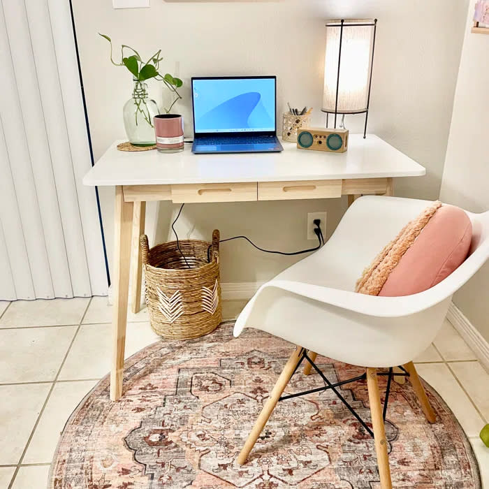 Reviewer's photo of the desk in the color white, decorated with a plant, a desk lamp, a small speaker, and a laptop, with a white chair and pink pillow in front of it