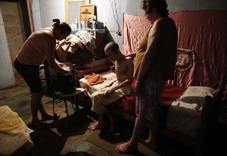 Cerebrovascular accident (CVA) patient Pedro, sits on his bed before being washed with the help of his daughter Daniela (L), 38, and wife Maria Do Carmo, 70, inside their house in Brasilandia slum, of which they are without water for 13 hours a day, in Sao Paulo February 11, 2015. REUTERS/Nacho Doce