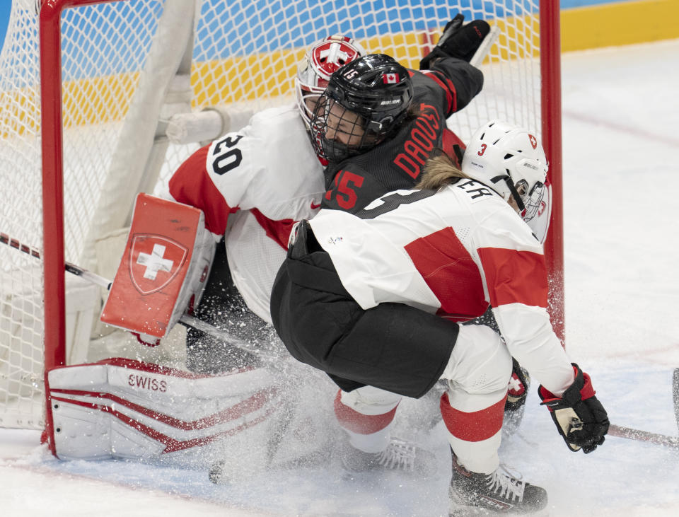 Canada forward Melodie Daoust (15) runs into Switzerland goalkeeper Andrea Braendli (20) as Switzerland defender Sarah Forster (3) moves in during the first period of a women's hockey game Thursday, Feb. 3, 2022, at the Winter Olympics in Beijing. (Ryan Remiorz/The Canadian Press via AP)