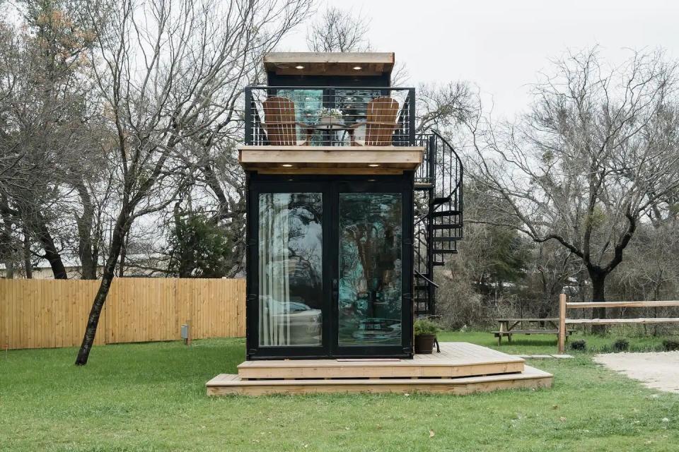a small black structure with a glass door and a metal frame on a grass lawn with trees and