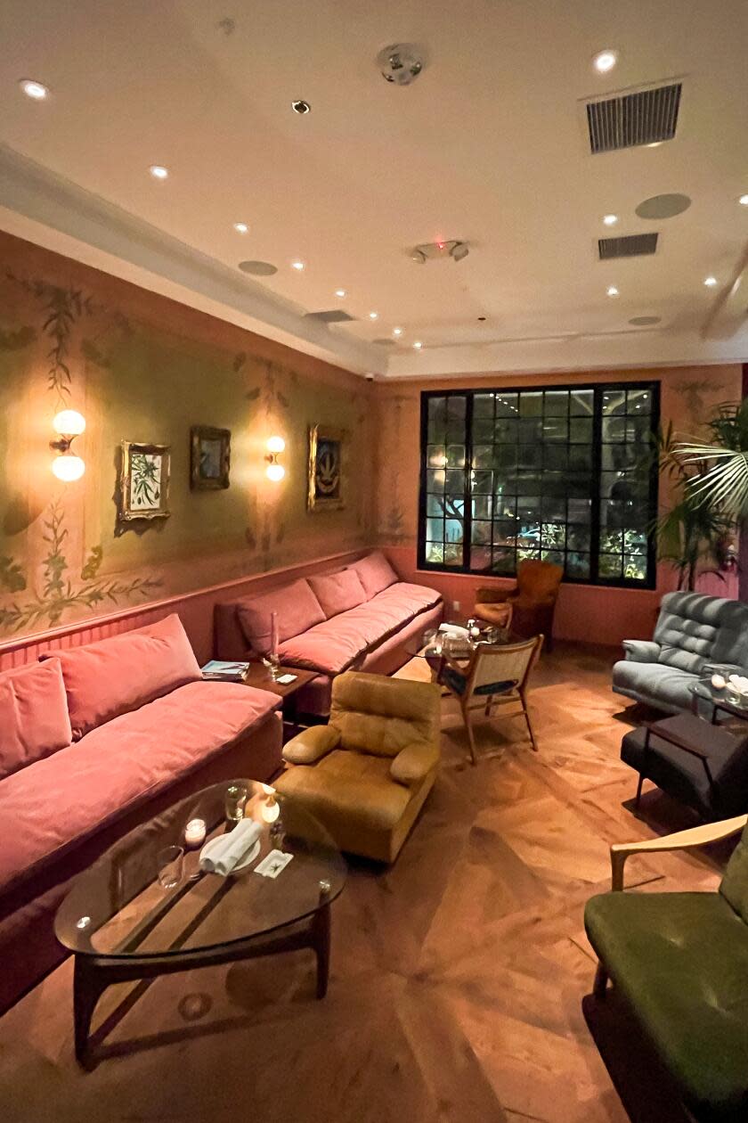 An empty lounge area with wooden floors, pink couches and floral wallpaper.