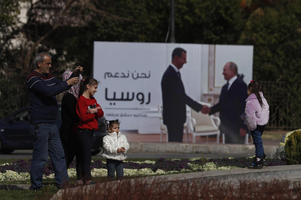 A family stands by a billboard showing Russian President Vladimir Putin and Syrian President Bashar Assad in Damascus, Syria, Monday, March 7, 2022. The Arabic in poster reads, "We support Russia." (AP Photo/Omar Sanadiki)