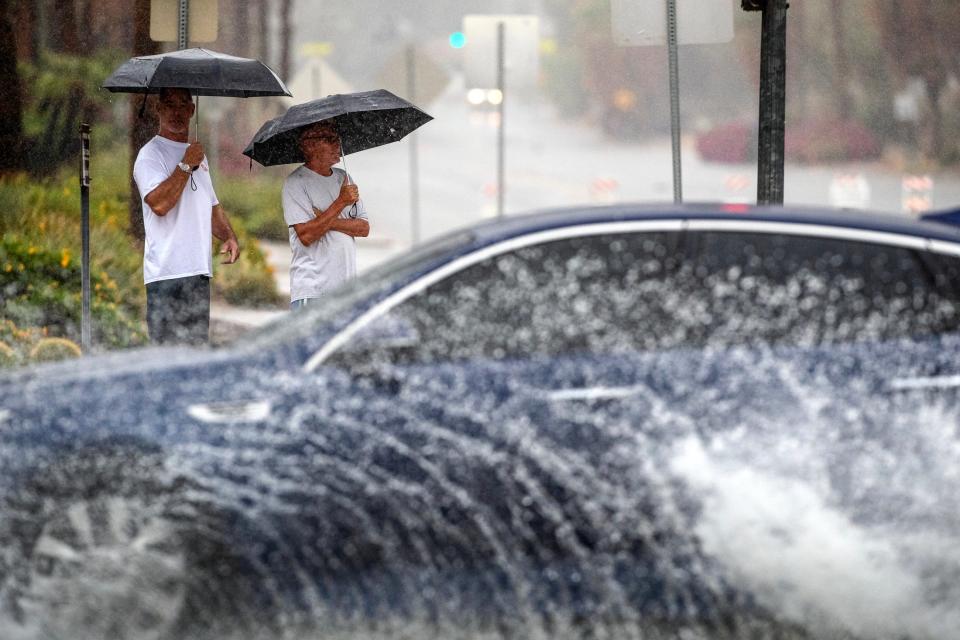 Jeff Larsen, left, and Robbie Jones watch cars drive on flooded streets Sunday during Tropical Storm Hilary in Palm Springs.