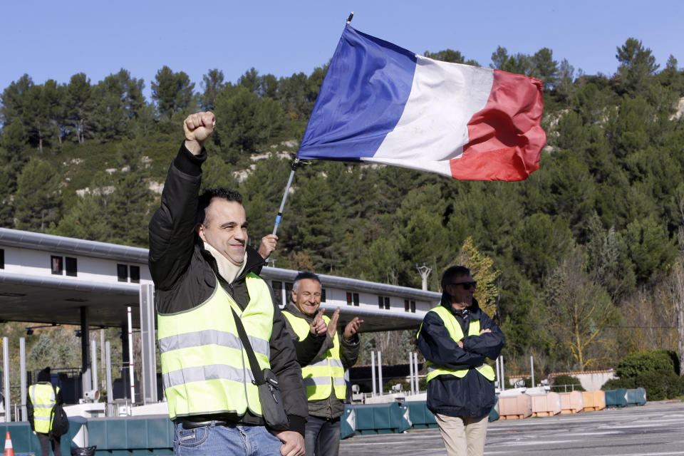 A demonstrators wearing a yellow vest clenches his fist as protesters open the toll gates on a motorway near Aix-en-Provence, southeastern France, Tuesday, Dec. 4, 2018. French Prime Minister Edouard Philippe announced a suspension of fuel tax hikes Tuesday, a major U-turn in an effort to appease a protest movement that has radicalized and plunged Paris into chaos last weekend. (AP Photo/Claude Paris)