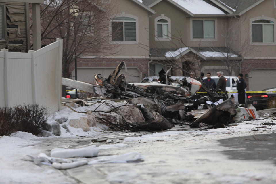 Firefighters and other investigators look at the debris from a small private plane that crashed in a residential area Wednesday, Jan. 15, 2020, in Roy, Utah. The small plane crashed Wednesday, killing the pilot as the aircraft narrowly avoided hitting any townhomes, authorities said. (Ben Dorger/Standard-Examiner via AP)