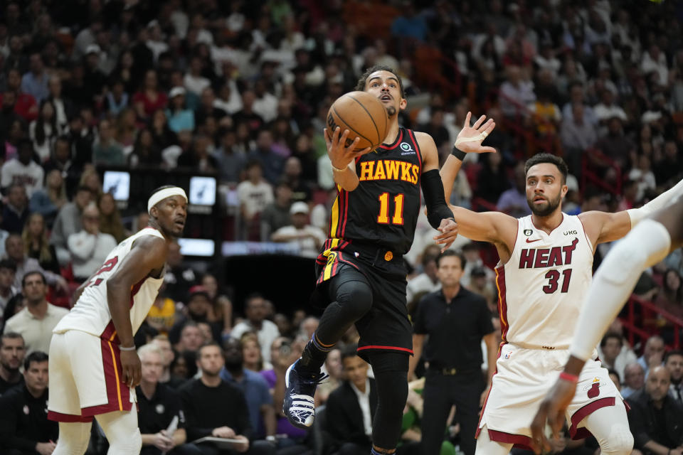 Atlanta Hawks guard Trae Young (11) looks for an opening past Miami Heat guard Max Strus (31) and forward Jimmy Butler, left, during the first half of an NBA basketball play-in tournament game Tuesday, April 11, 2023, in Miami. (AP Photo/Rebecca Blackwell)