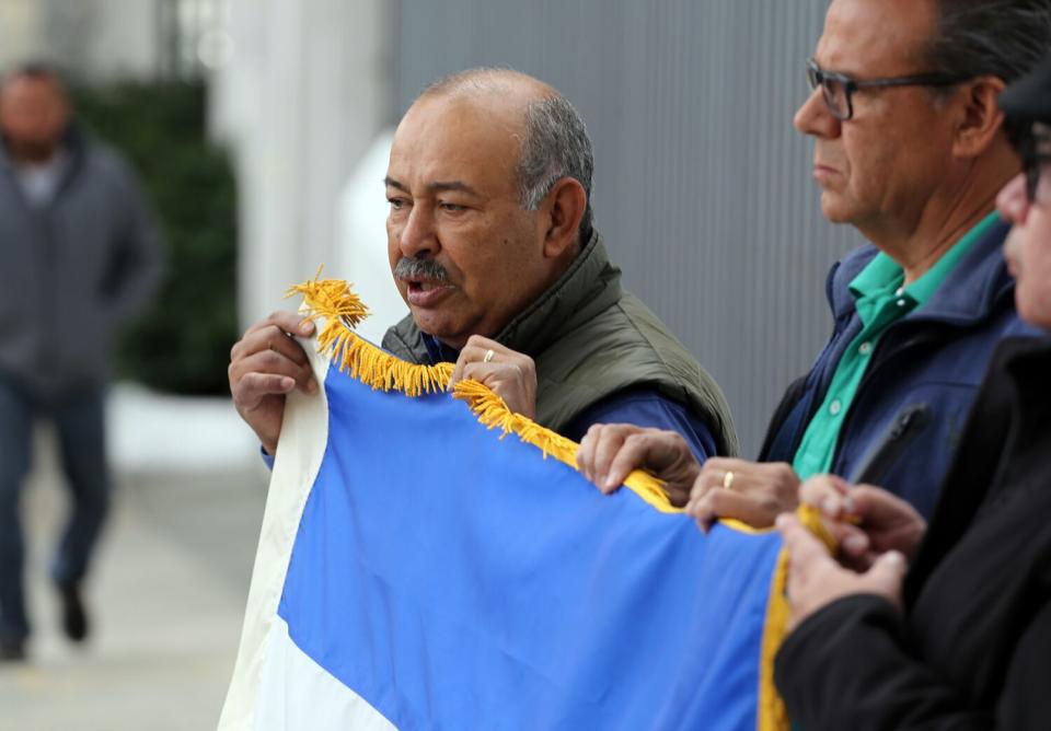 Three people hold a blue and white flag.