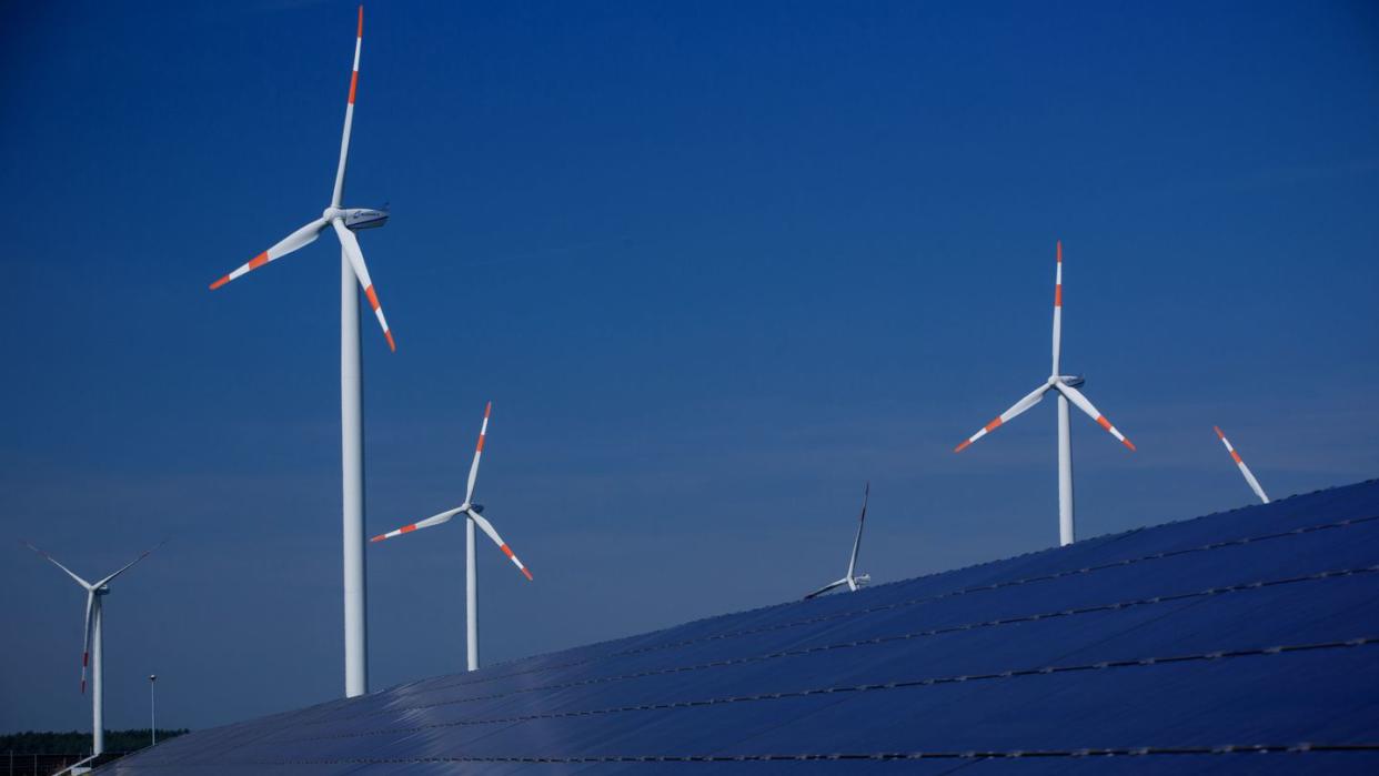 Windräder zur Stromerzeugung drehen sich in Mecklenburg-Vorpommern hinter einem Solarpark.