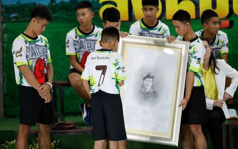 The boys hold a portrait of Saman Gunan, the Thai SEAL diver who died during their rescue - Credit: AP