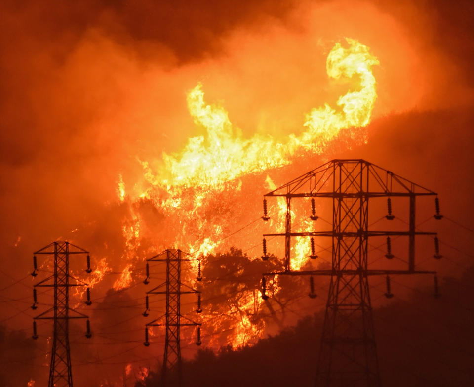 FILE - In this Dec. 16, 2017, file photo provided by the Santa Barbara County Fire Department, flames burn near power lines in Sycamore Canyon near West Mountain Drive in Montecito, Calif. Pacific Gas & Electric said it will shut off power Saturday, June 8, to about 1,600 customers in Northern California and may do the same for thousands more to reduce the risk of wildfires. The utility announced Friday night that as of Saturday morning it will turn off electricity to customers in Napa, Solano and Yolo counties west of Sacramento. (Mike Eliason/Santa Barbara County Fire Department via AP, File)