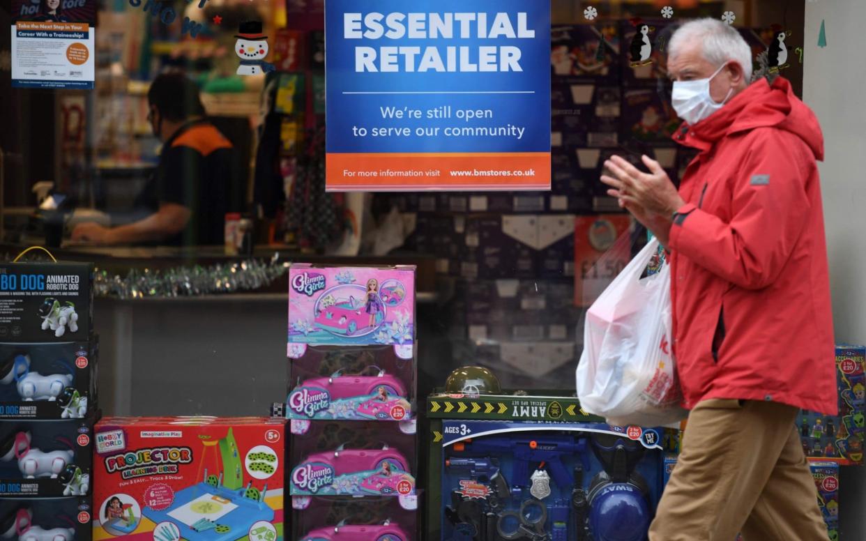 A man wearing a protective face covering walks past a store declaring itself an "essential retailer" in Ashton-under-Lyne east of Manchester in north-west England on November 11, 2020, as people in England live through a second nationwide lockdown to combat the spread of the novel coronavirus covid-19. - A united effort to tackle spiking coronavirus infection rates has been called for as 56 million people in England went into a second lockdown but with the public weary of restrictions and fearing for their livelihoods. (Photo by Oli SCARFF / AFP) (Photo by OLI SCARFF/AFP via Getty Images)  - Oli Scarff/AFP