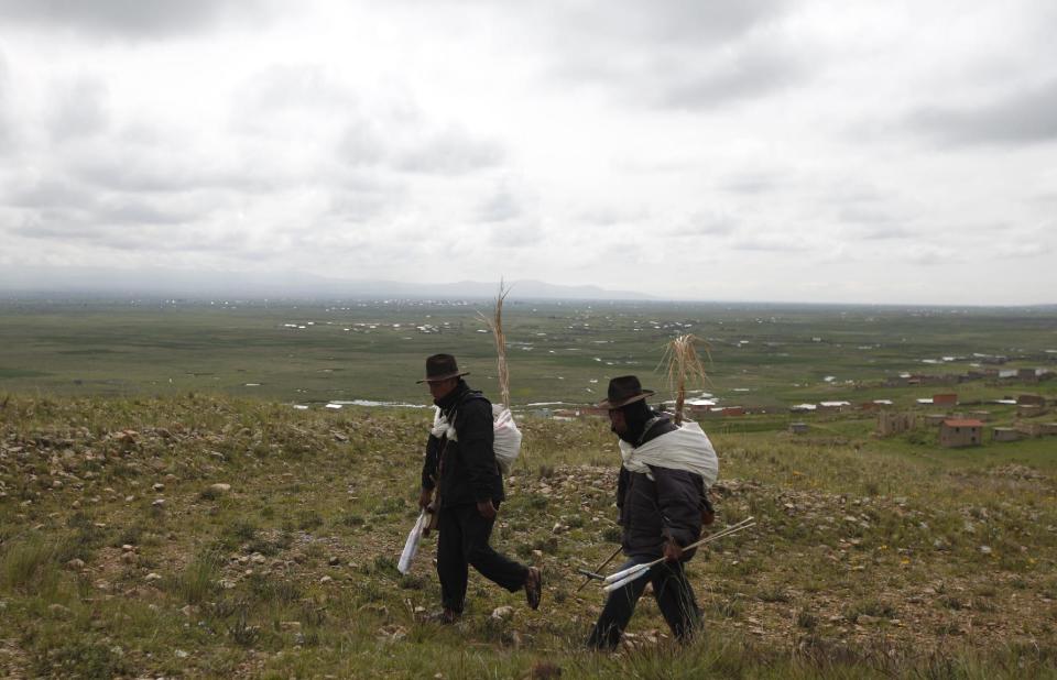 In this Feb. 14, 2014 photo, Aymara Indians walk to the top of a hill to demonstrate how they blow their horns to warn residents of storms in Cutusuma, Bolivia. For centuries, farmers in the fragile ecosystems of the high Andes have looked to the behavior of plants and animals to figure out what crops to grow and when. (AP Photo/Juan Karita)