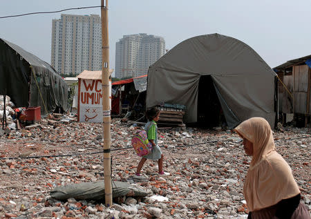A student walks near a temporary shelter for people after her house was demolished last year, in Luar Batang area in Jakarta, Indonesia April 18, 2017. REUTERS/Beawiharta