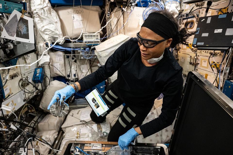 two women in sweat suits unpack a large metal box in a cramped laboratory full of wires and computers. they are floating