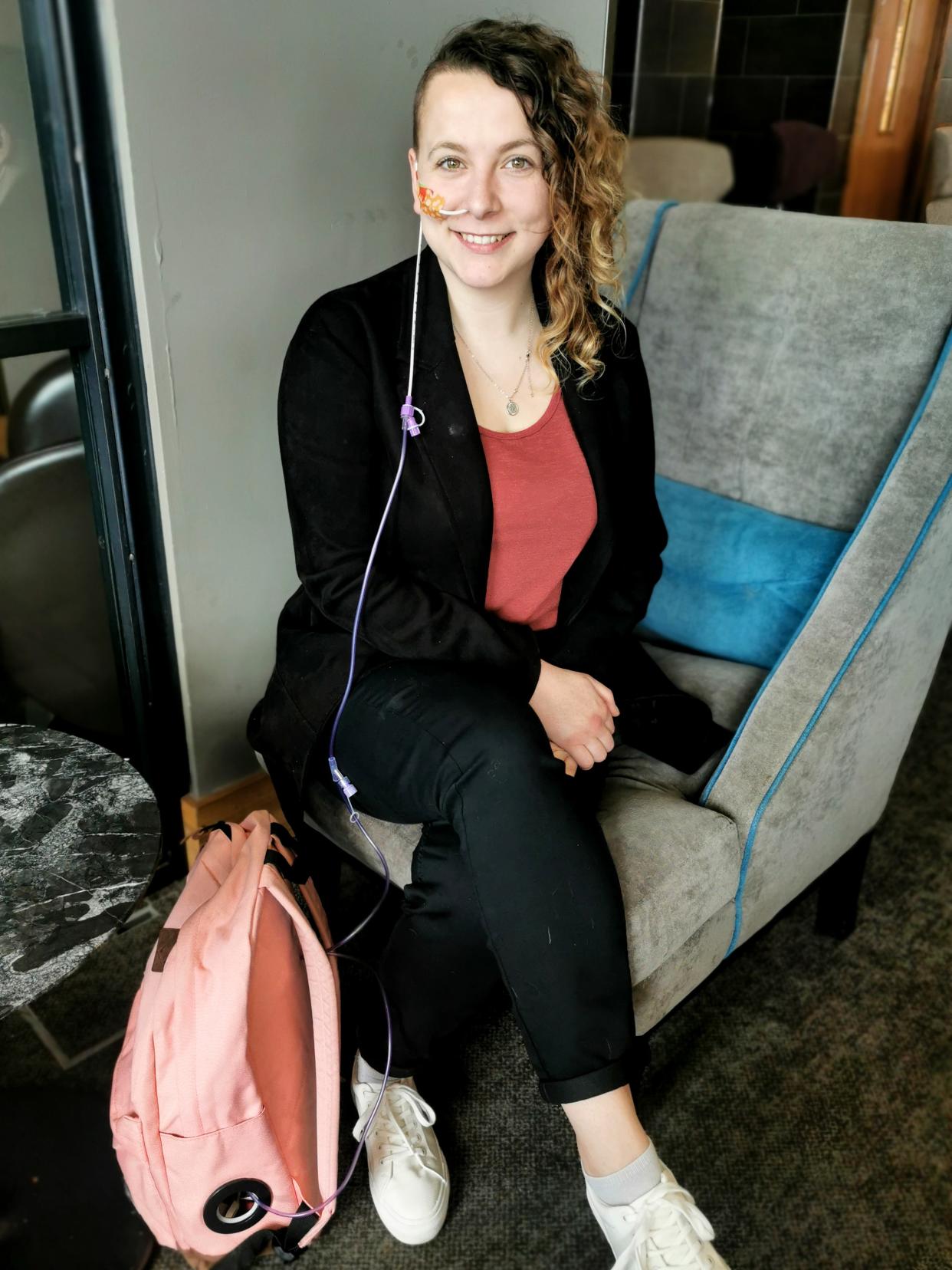 Bingham sits on a chair wearing her feeding tube