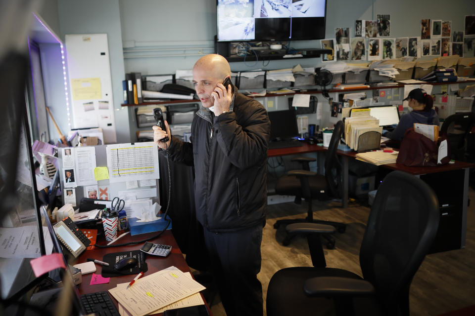 Pat Marmo, owner of Daniel J. Schaefer Funeral Home, speaks on two phones at once in his office while handling the overflow of clients stemming from COVID-19 deaths, Thursday, April 2, 2020, in the Brooklyn borough of New York. Like many funeral homes in New York and around the globe, Marmo's business is in crisis. His office phone and two mobiles are ringing constantly. He's apologizing to families at the start of every conversation for being unusually terse and insensitive, and begging them to insist hospitals hold their loved ones as long as possible. (AP Photo/John Minchillo)