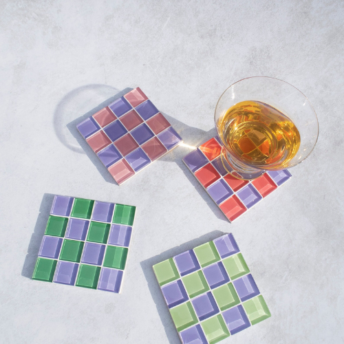 four checkerboard coasters with a glass on one