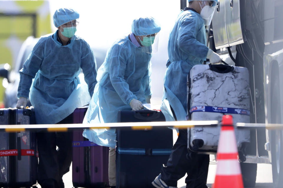 Staffs in protective suits load to a bus the luggages of the foreign passengers disembarked from the quarantined Diamond Princess cruise ship before boarding to buses at a port in Yokohama, near Tokyo, Friday, Feb. 21, 2020. Passengers tested negative for COVID-19 started disembarking since Wednesday. (AP Photo/Eugene Hoshiko)