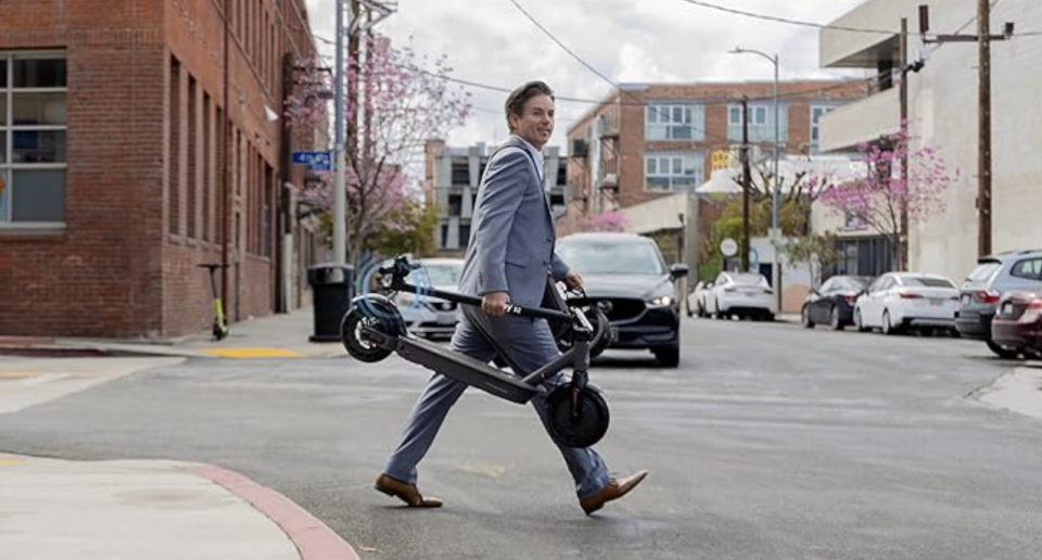a person walking in a city with a folded scooter