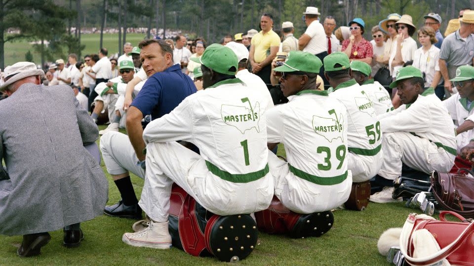 Arnold Palmer looks over his shoulder as he sits with a group of caddies during the 1965 Masters. - Augusta National/Getty Images