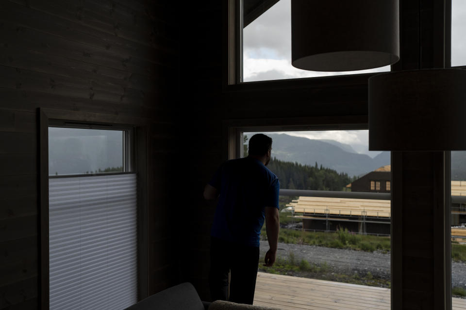 Garrett Fisher checks the weather conditions through the window of a rented house in Voss, Norway, on Aug. 3, 2022. Fisher brings in his iPad for navigation, but his aviation software doesn't have GPS information on glaciers. He flies using a mix of instinct, observation and Google Maps. (AP Photo/Bram Janssen)