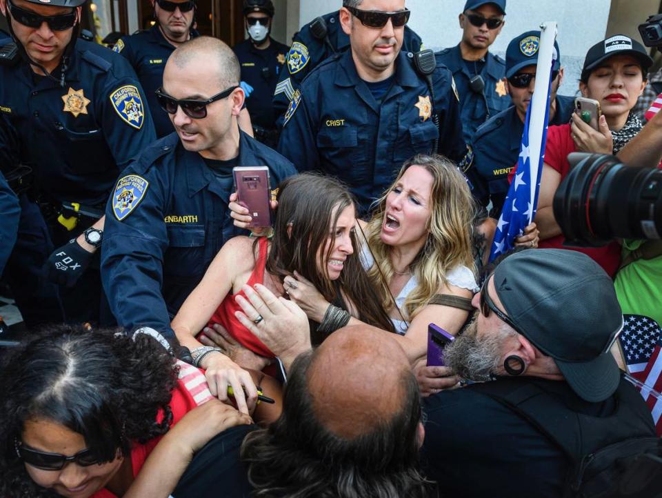 Protester Heidi Munoz Gleisner, left, was removed from a demonstration against Gov. Gavin’s Newsom’s stay-at-home order by California Highway Patrol officers after they ordered a crowd of people to leave the Capitol grounds Friday, May 1, 2020. 