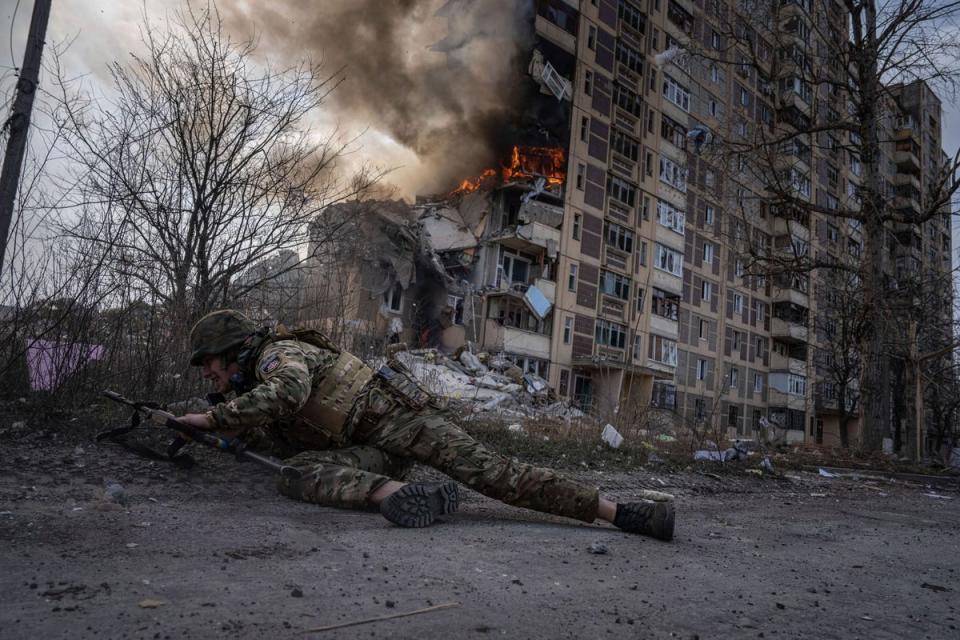 A Ukrainian police officer takes cover in front of a burning building that was hit in a Russian airstrike in Avdiivka (AP)