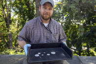 This photo, provided by the U.S. Military Academy at West Point, Aug. 30, 2023, shows West Point archeologist Paul Hudson displaying coins found in the lead box believed to have been placed in the base of a monument by cadets almost two centuries ago, in West Point, NY. The nearly 200-year-old West Point time capsule, that appeared to yield little more than dust when it was opened during a disappointing livestream earlier this week, contained hidden treasure after all, the U.S. Military Academy said Wednesday. (U.S. Military Academy at West Point via AP)