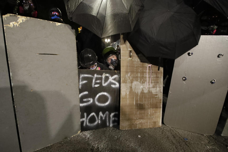 Demonstrators shield themselves from federal officers during a Black Lives Matter protest at the Mark O. Hatfield U.S. Courthouse on Saturday, July 25, 2020, in Portland, Ore. On the streets of Portland, a strange armed conflict unfolds night after night. It is raw, frightening and painful on both sides of an iron fence separating the protesters on the outside and federal agents guarding a courthouse inside. This weekend, journalists for The Associated Press spent the weekend both outside, with the protesters, and inside the courthouse, with the federal agents, documenting the fight that has become an unlikely centerpiece of the protest movement gripping America. (AP Photo/Marcio Jose Sanchez)