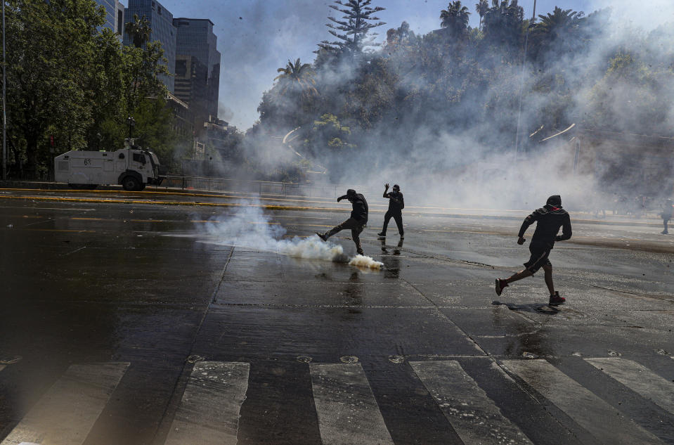 A protester kicks back tear gas fired by police trying to disperse a march against the commemoration of the discovery of the Americas, organized by indigenous groups demanding autonomy and the recovery of ancestral land in Santiago, Chile, Monday, Oct. 12, 2020. (AP Photo/Esteban Felix)